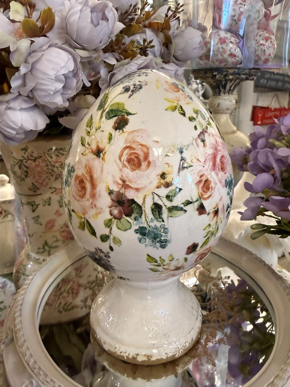 Œuf décoratif fleuri style Liberty avec roses et feuillages dans des tons rose et vert sur fond ivoire, posé sur un socle patiné, décoration romantique shabby chic pour intérieur de charme.