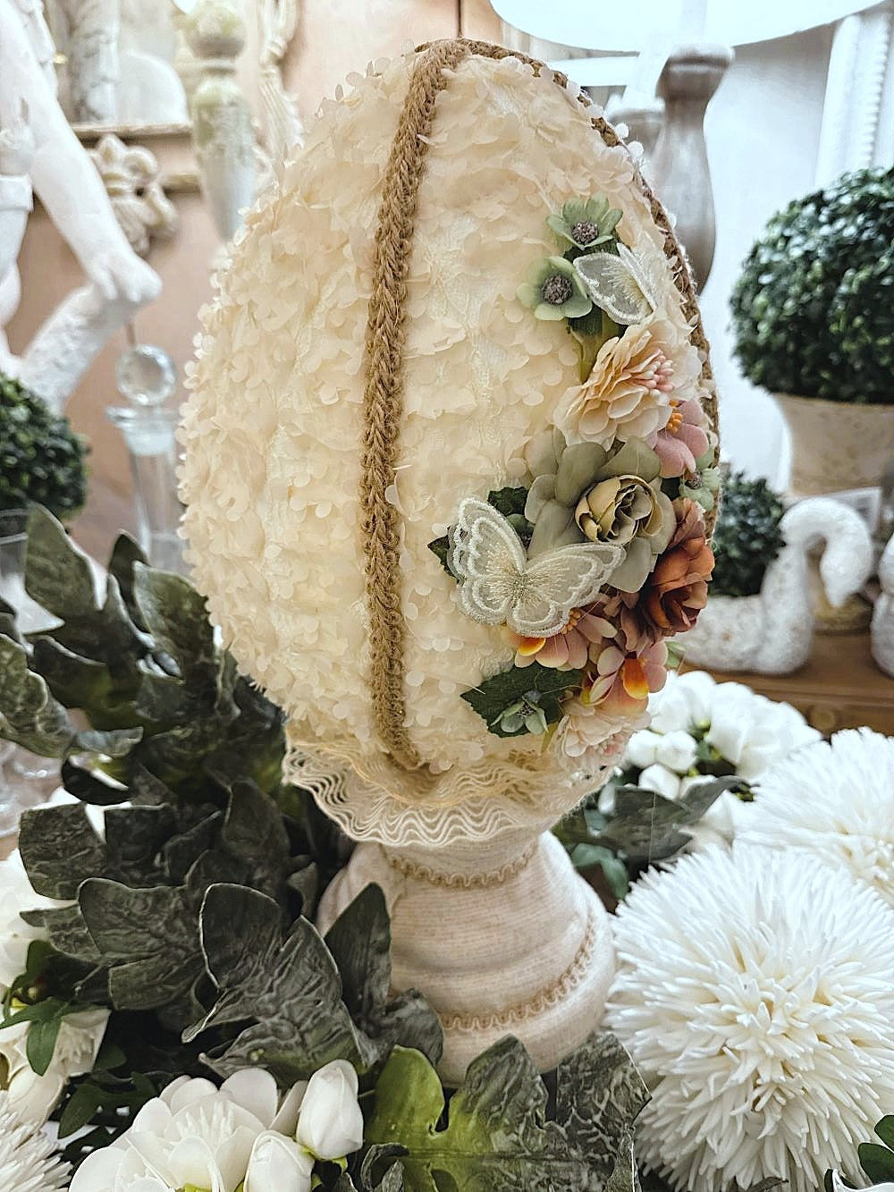 Œuf décoratif en style shabby chic orné de fleurs en tissu et de papillons, dans les tons ivoire, vieux rose et vert sauge, pour une ambiance romantique et poétique.