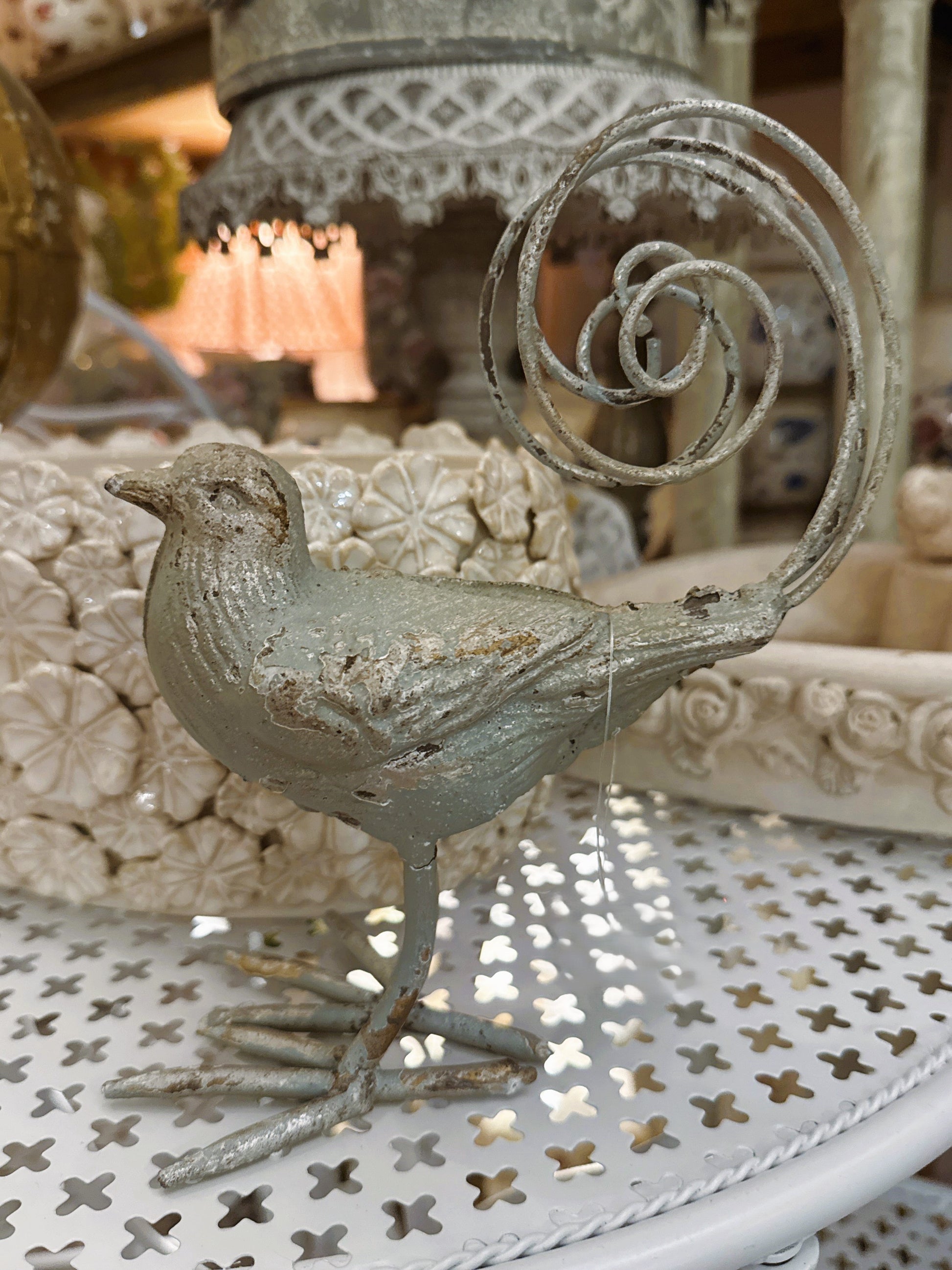 Oiseau décoratif en métal argent vieilli avec queue en spirale, style romantique et shabby chic, dimensions 18x10,5x20 cm, posé sur une table blanche ajourée.