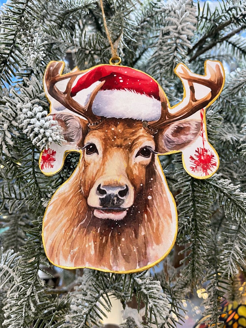 Ornement Renne Festif en métal, vu de face dans un sapin enneigé.