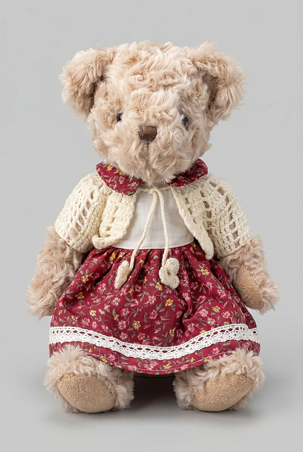 Oursonne décorative en peluche beige vêtue d’une robe fleurie rouge et d’un gilet crocheté écru, style shabby chic romantique pour chambre ou décoration de charme