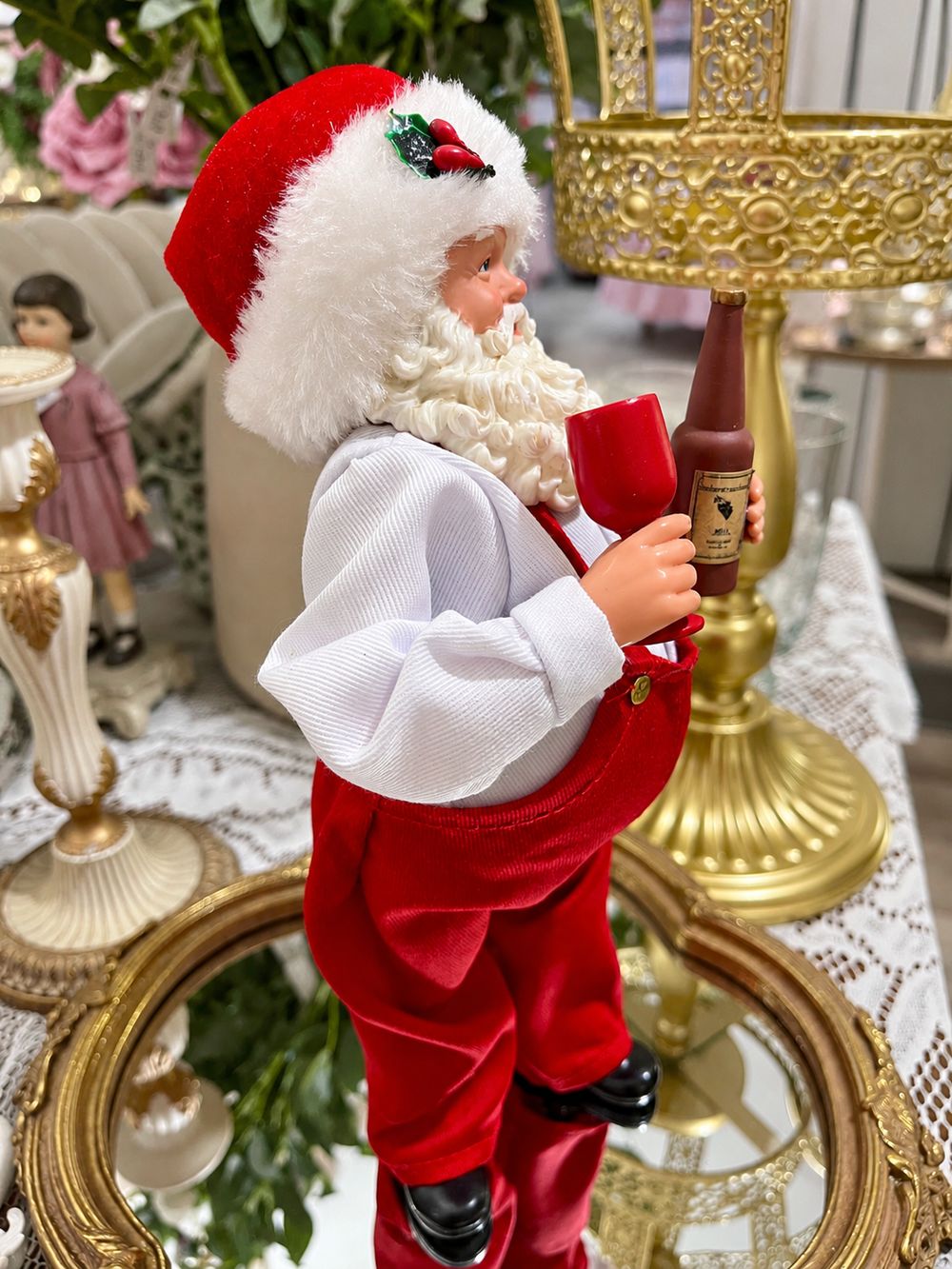 Vue de profil du Père Noël Esprit des Vignes avec son bonnet à houx, son verre rouge et sa bouteille miniature.