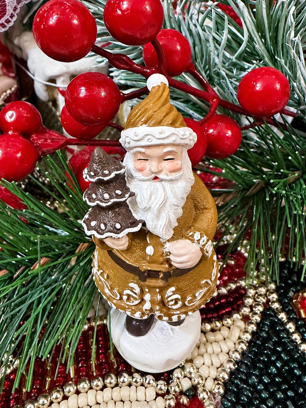 Père Noël Pain d’Épices Miniature vu de face parmi des branches de sapin et des baies rouges.