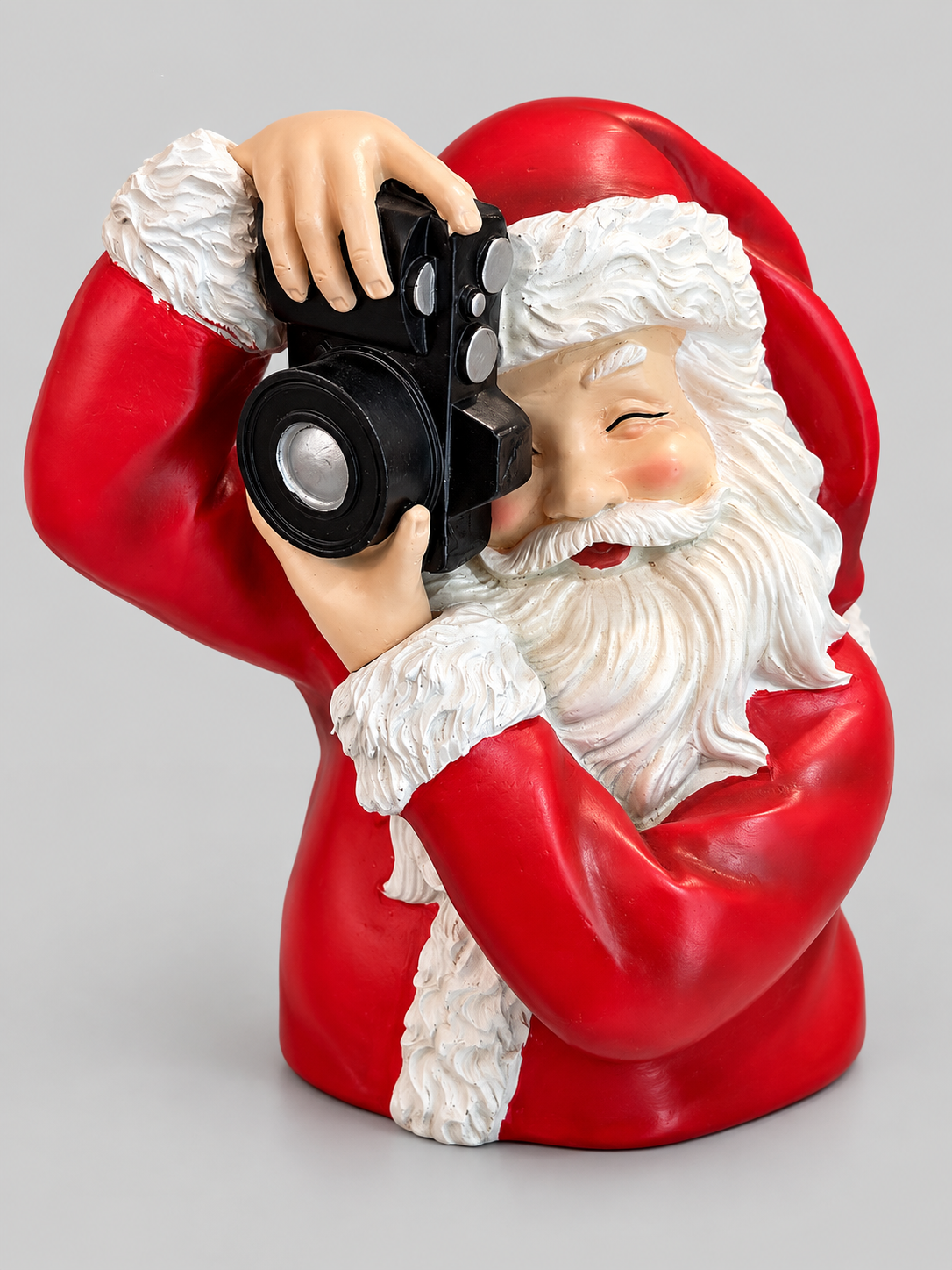 Figurine Père Noël rouge et blanc tenant un appareil photo noir, présentée sur fond gris clair