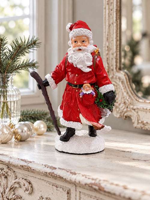 Figurine Père Noël Randonnée sur une console blanche patinée, près d’un miroir ancien et de boules de Noël.