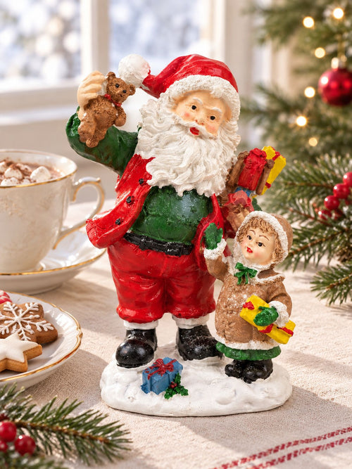 Figurine Père Noël et enfant sur une table de Noël, près d’une tasse de chocolat chaud et de biscuits décorés.