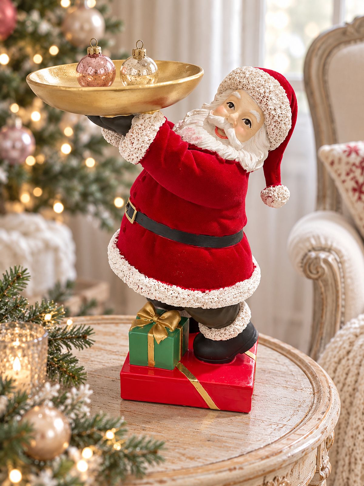 Père Noël serviteur portant deux petites boules de Noël dans son plateau, près d’un fauteuil et d’un sapin.