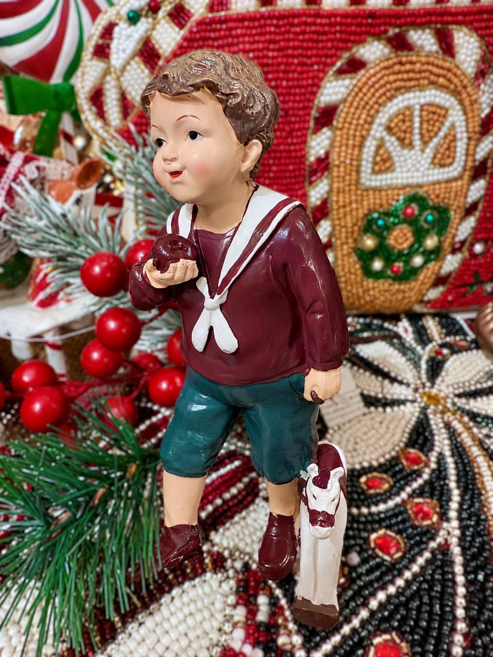 Figurine Petit Garçon au Cheval vue de trois quarts, en tenue bordeaux et verte, dans un décor de Noël.