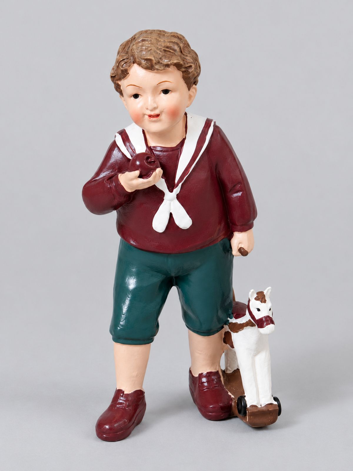Figurine Petit Garçon au Cheval en tenue bordeaux et verte, accompagnée de son cheval miniature, sur fond gris clair.