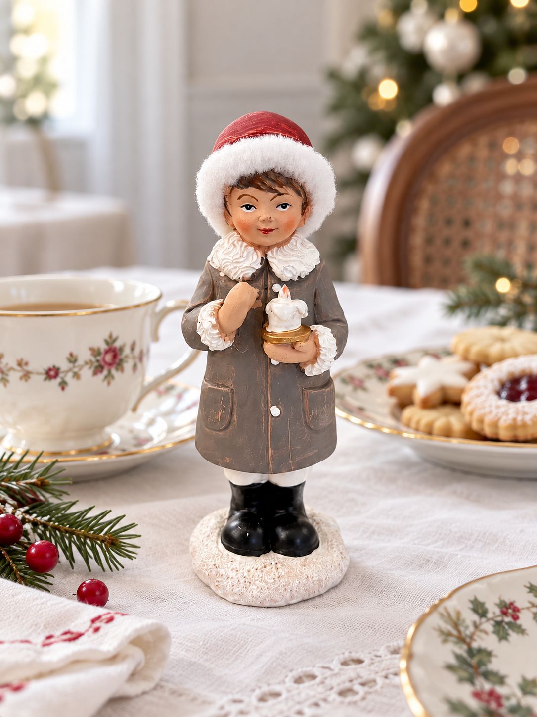 Figurine de petit garçon à la bougie sur une table de Noël, près d’une tasse fleurie et de biscuits.