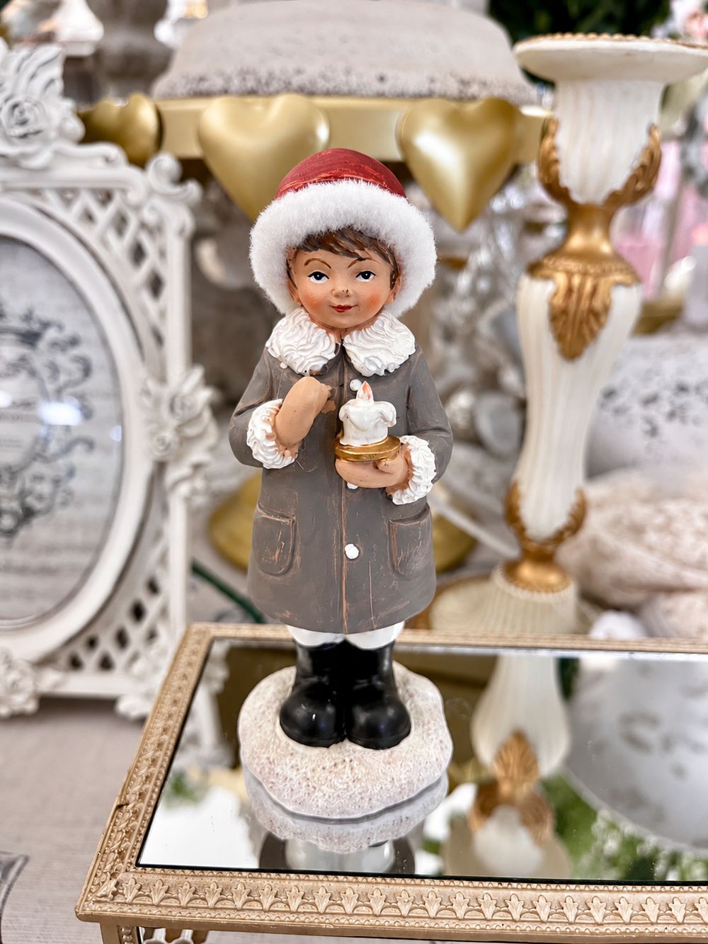 Figurine de petit garçon à la bougie vue de face, avec bonnet rouge, manteau gris patiné et socle clair.