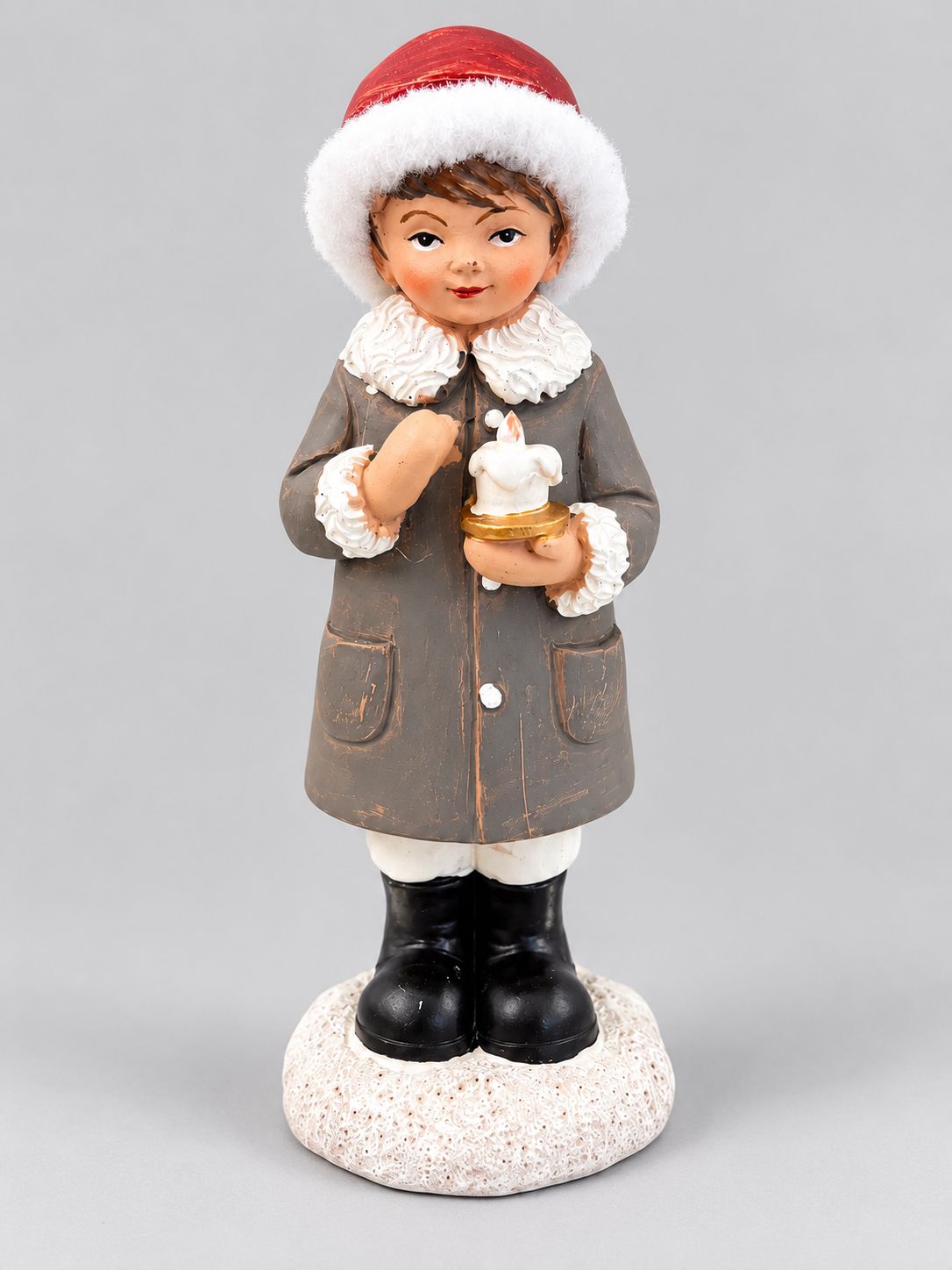 Figurine de petit garçon tenant une bougie, avec bonnet rouge et manteau gris patiné, sur fond gris clair.