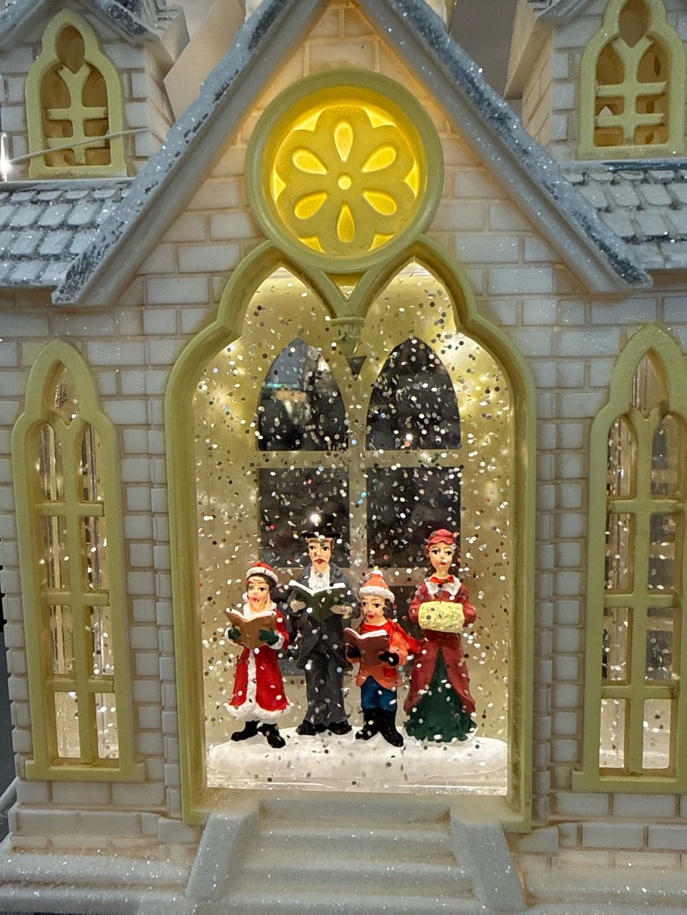 Chapelle de Noël lumineuse avec chorale miniature, éclairage chaleureux et paillettes animées, décoration féérique de village de Noël romantique