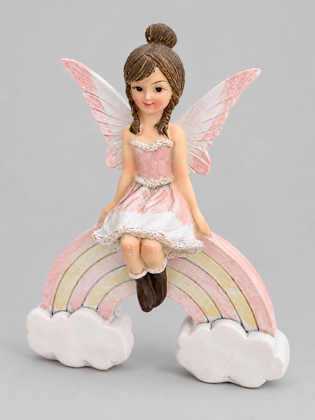 Figurine de petite fée rose et blanche assise sur un arc-en-ciel pastel entre deux nuages, sur fond gris clair.