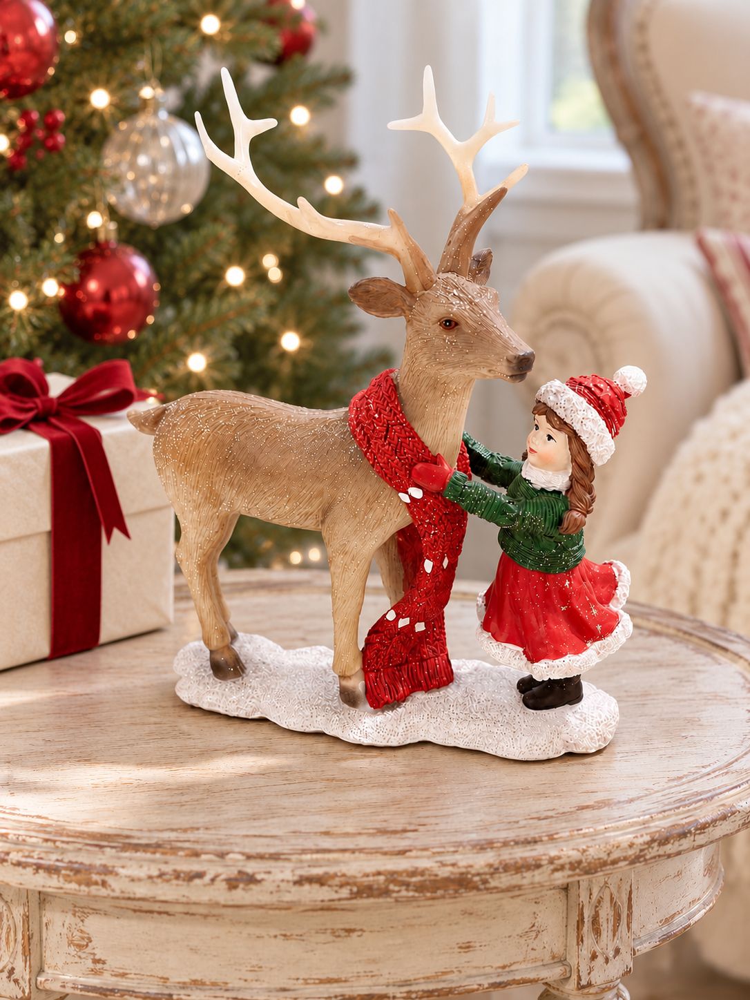 Figurine Petite Fille et Son Cerf sur une table patinée devant un sapin de Noël et un fauteuil crème.