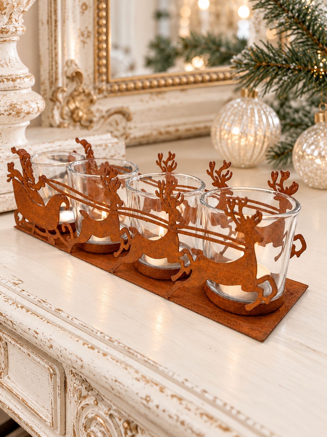 Photophore Traîneau du Père Noël avec quatre chauffe-plats allumés sur une console ivoire patinée devant un miroir ancien.