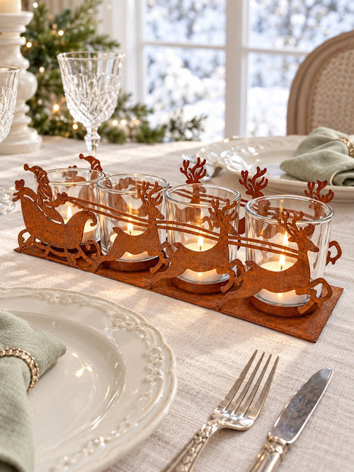 Photophore de Noël en métal effet rouille avec quatre chauffe-plats allumés sur une table en lin écru, entre des assiettes anciennes.