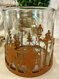 Photophore en verre 15x15 cm avec décor en métal rouille représentant une scène de village d’hiver, enfants, arbres et animaux, style romantique et féérique