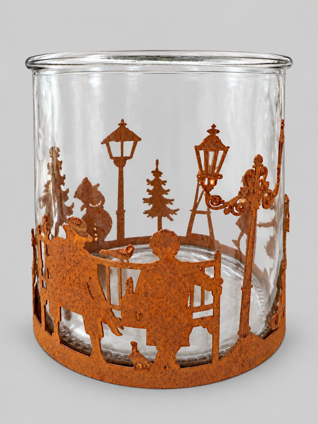 Photophore Village d’Hiver en verre transparent et métal patiné rouille sur fond gris clair.