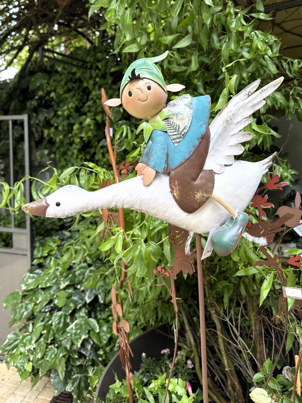 Décoration de jardin en métal représentant un lutin féérique bleu et vert sur une oie blanche en plein vol, style poétique et romantique, idéale pour un extérieur enchanteur