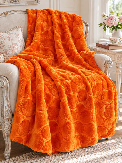 Plaid orange citrouille drapé sur un fauteuil écru près d’une table avec une tasse et des roses.
