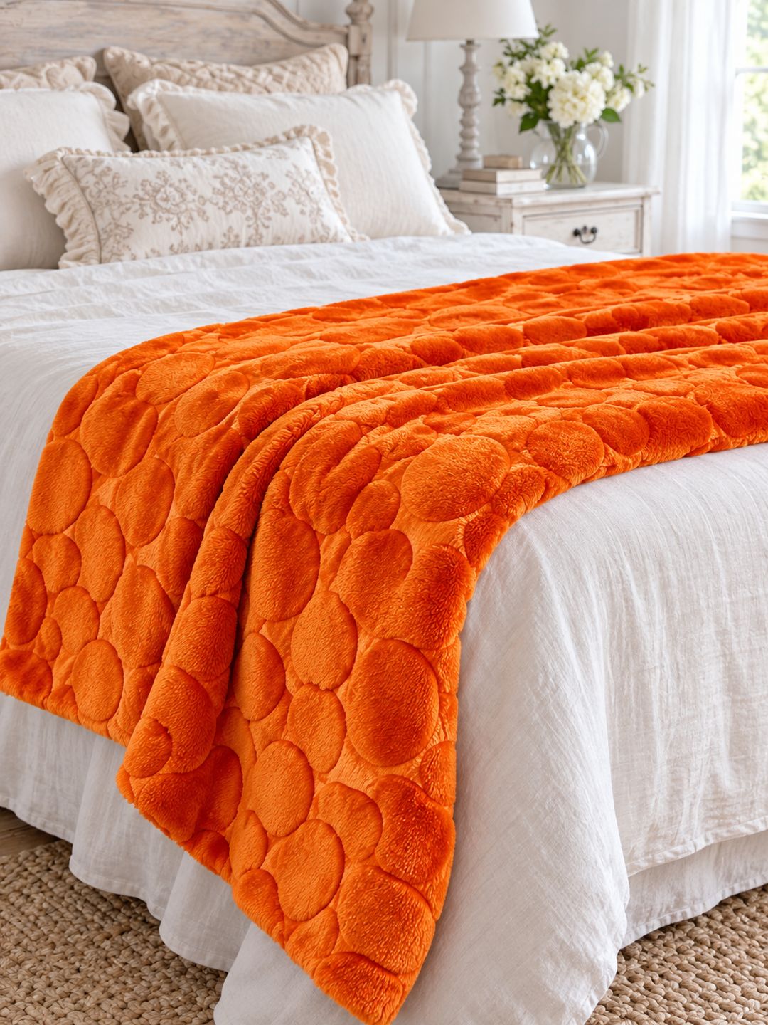 Plaid orange citrouille disposé au pied d’un lit habillé de linge blanc dans une chambre romantique.