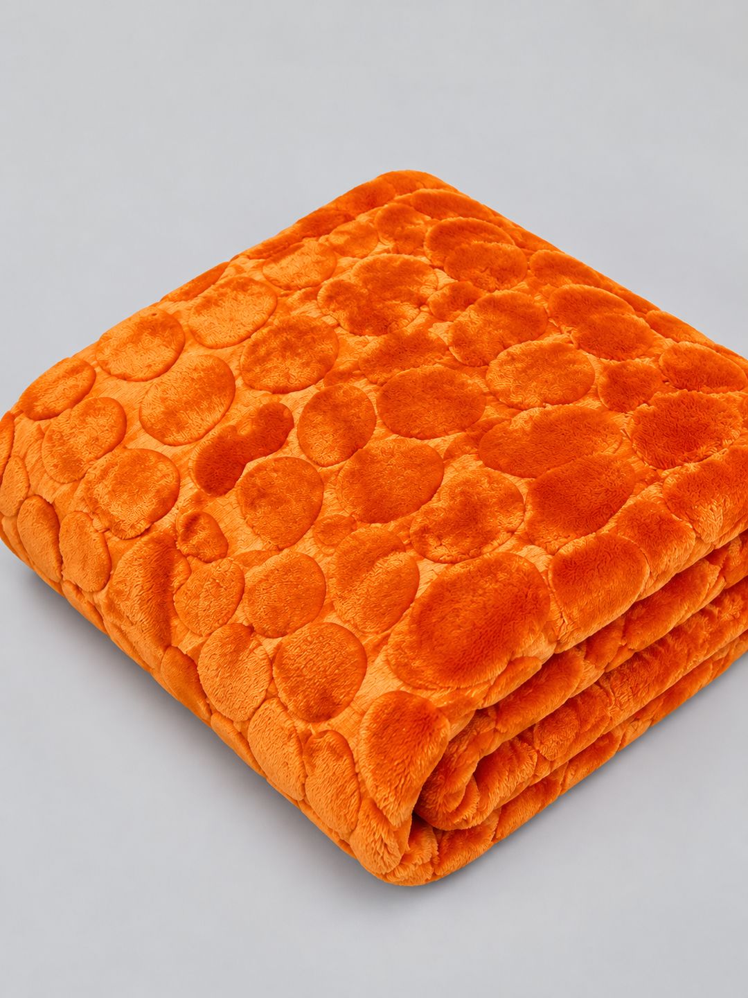 Plaid Douceur Citrouille plié, avec sa texture moelleuse et ses motifs en relief, sur fond gris clair.