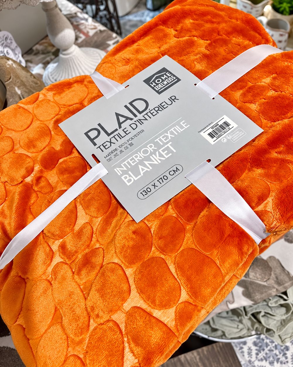Plaid Douceur Citrouille plié dans son emballage, avec sa texture moelleuse et ses motifs en relief.