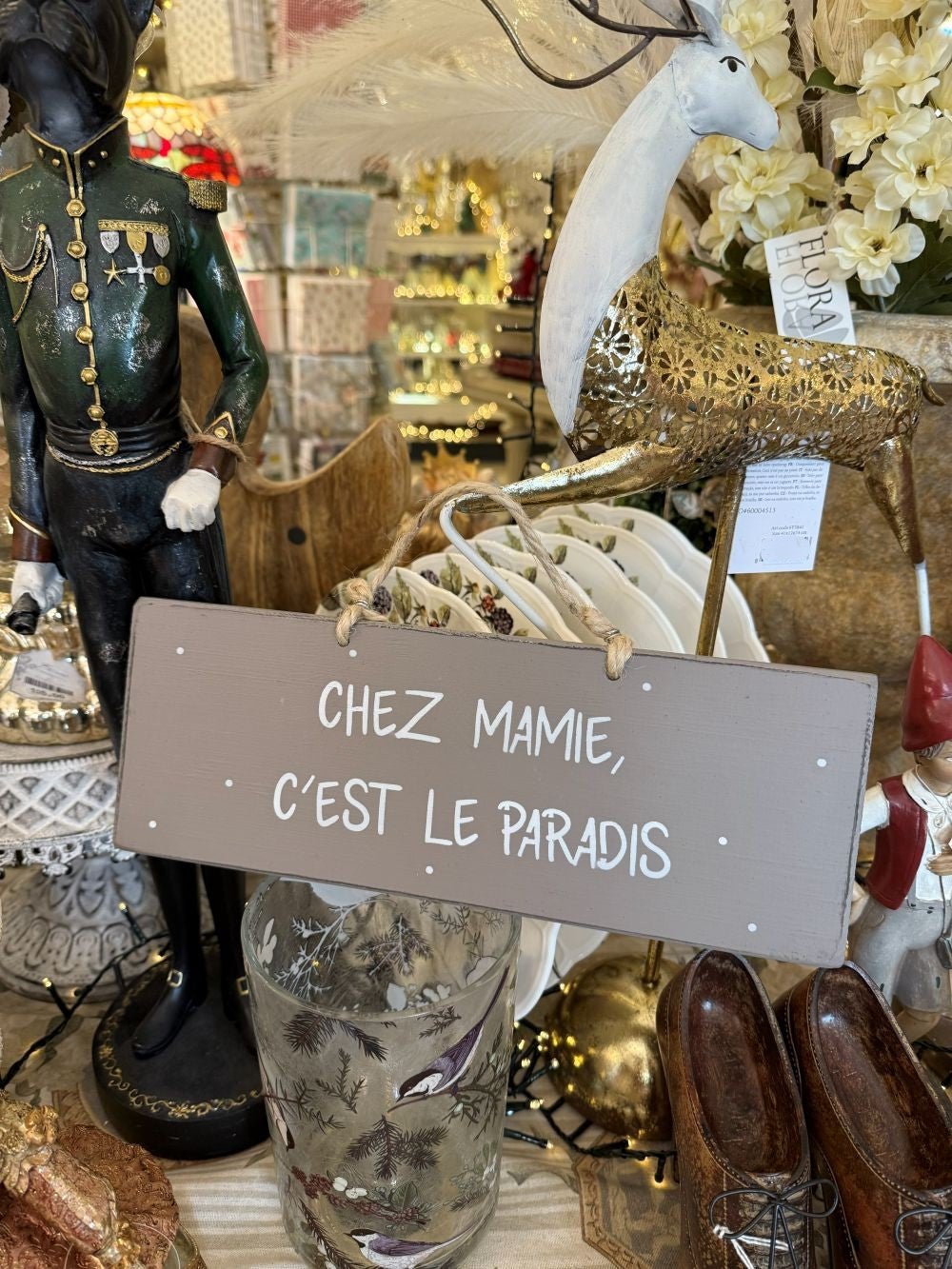 Plaque décorative en bois taupe avec inscription blanche « Chez Mamie c’est le paradis », style shabby chic, suspendue par une corde naturelle dans une ambiance romantique et chaleureuse