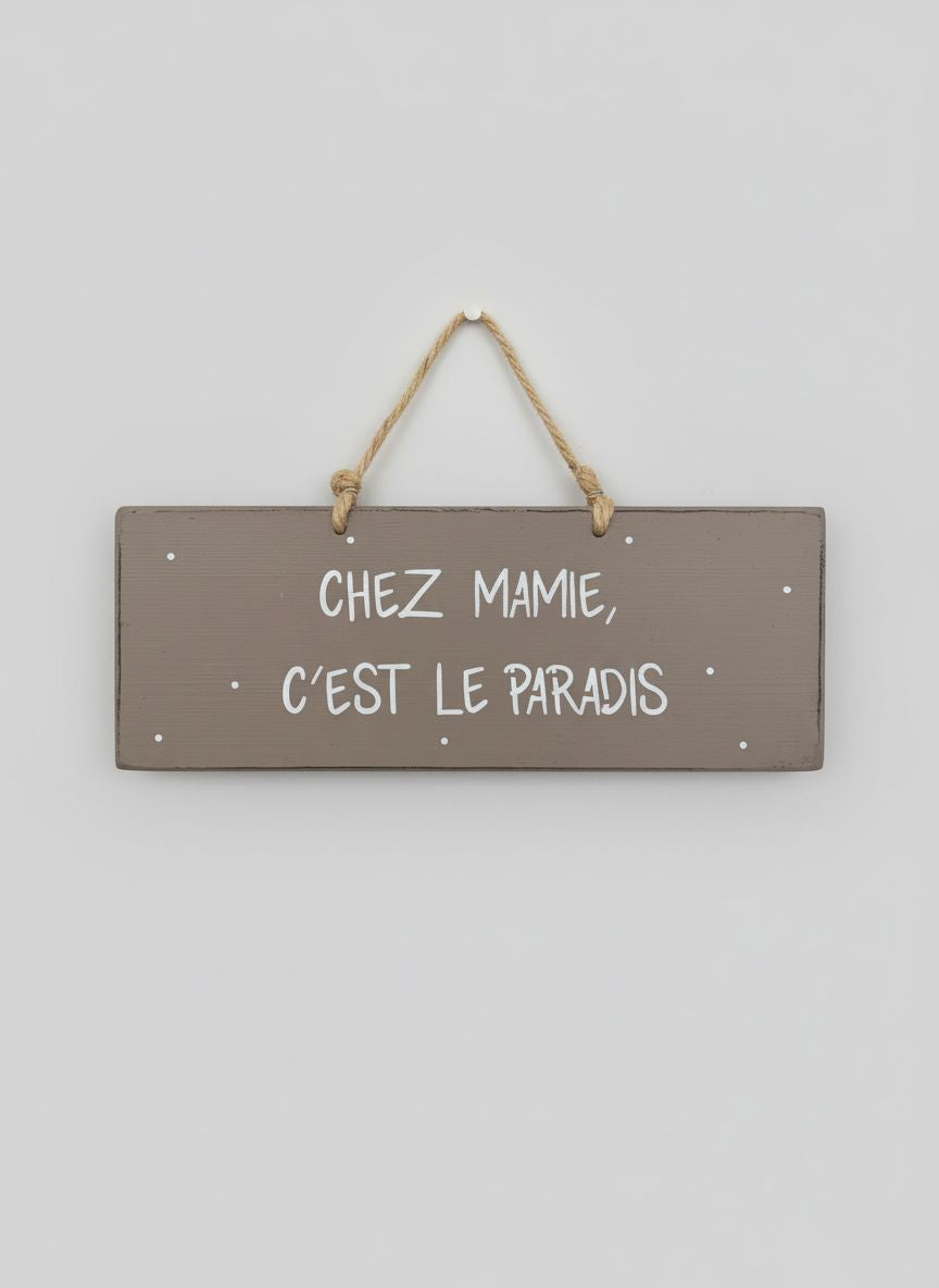 Plaque décorative en bois taupe avec inscription blanche « Chez Mamie c’est le paradis », style shabby chic, suspendue par une corde naturelle dans une ambiance romantique et chaleureuse
