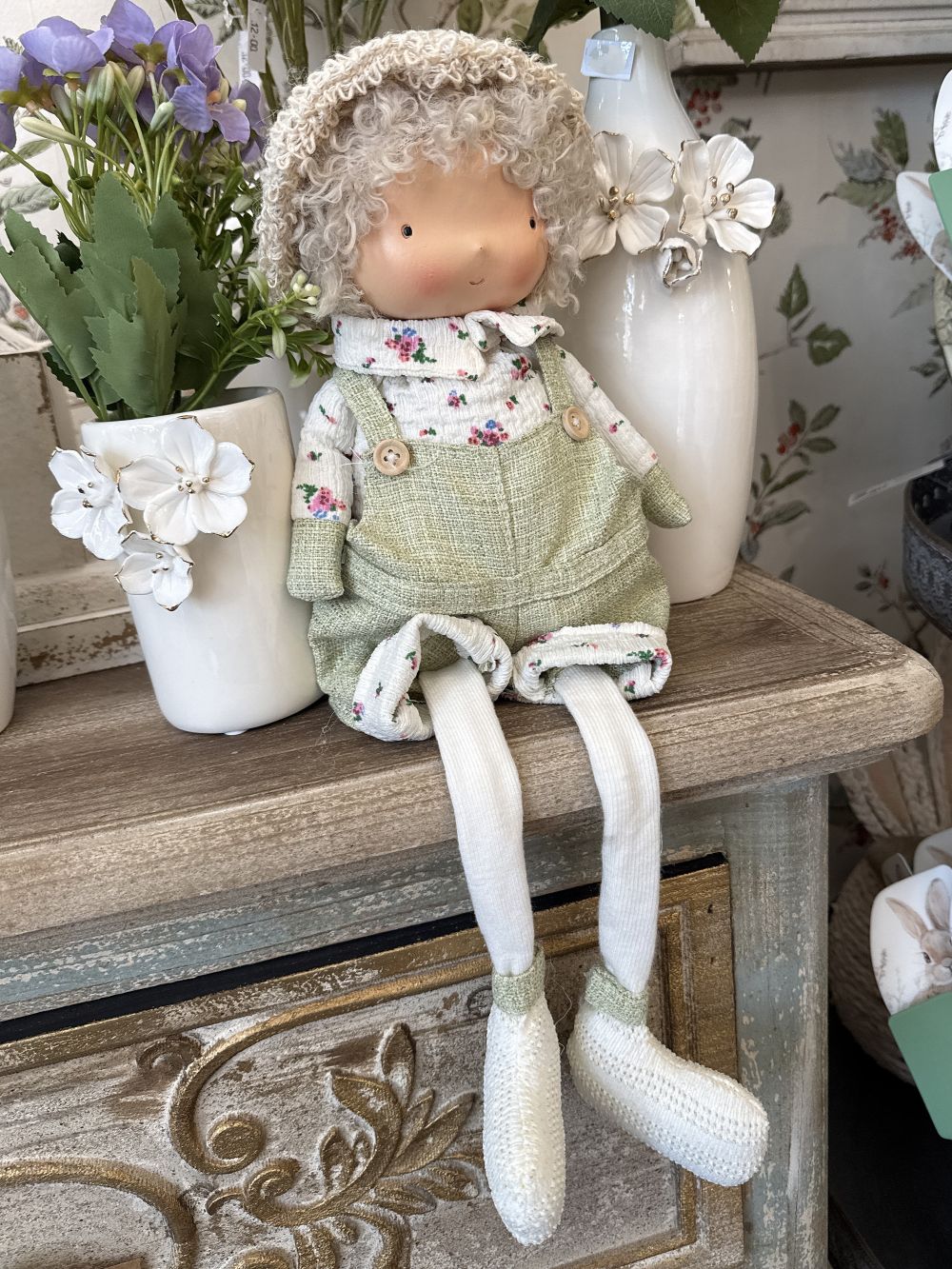 Poupée décorative assise Mr Printemps aux couleurs vert tendre, blanc et beige, style shabby chic romantique avec tenue florale et longues jambes pendantes pour décoration de charme printanière