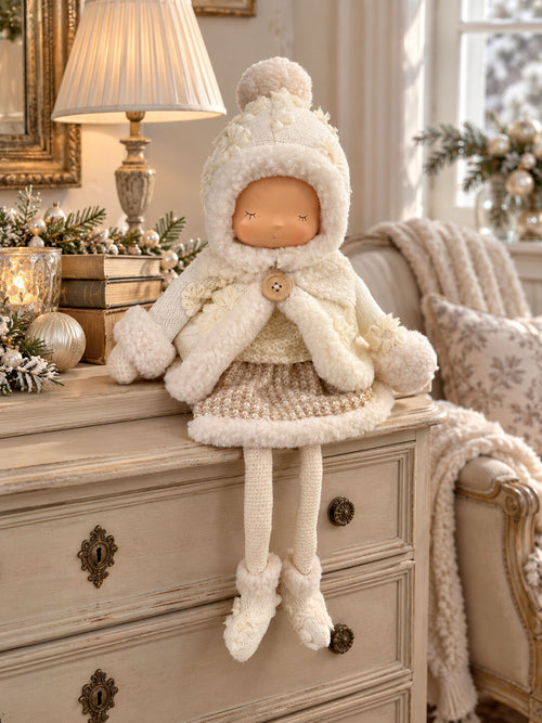 Grande poupée décorative d’hiver écrue et beige avec bonnet, tenue douillette et longues jambes, assise sur un meuble dans une ambiance shabby chic romantique