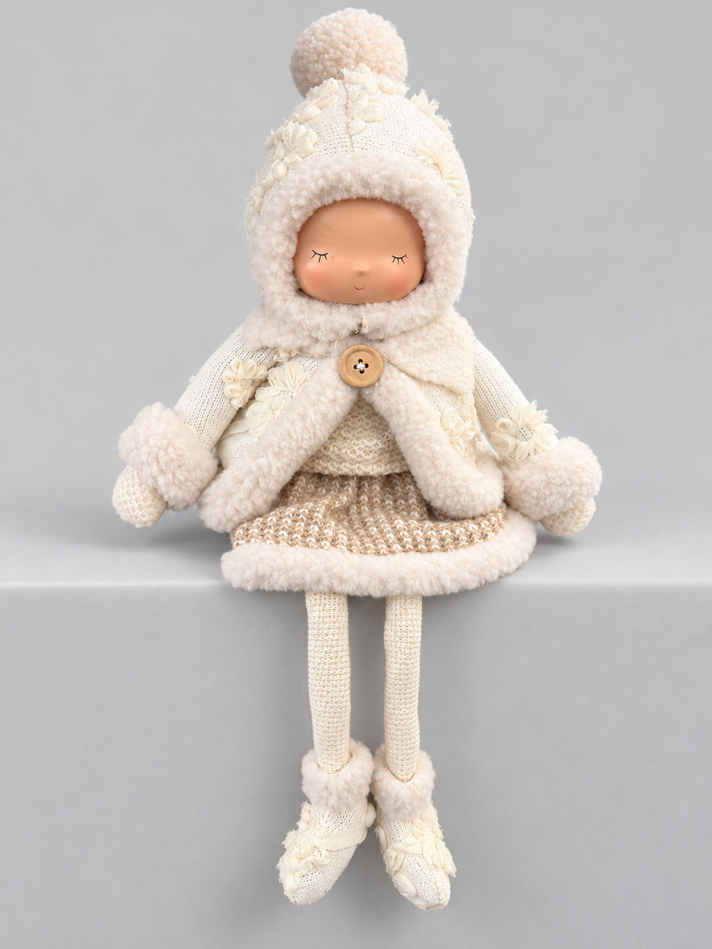 Grande poupée décorative d’hiver écrue et beige avec bonnet, tenue douillette et longues jambes, assise sur un meuble dans une ambiance shabby chic romantique