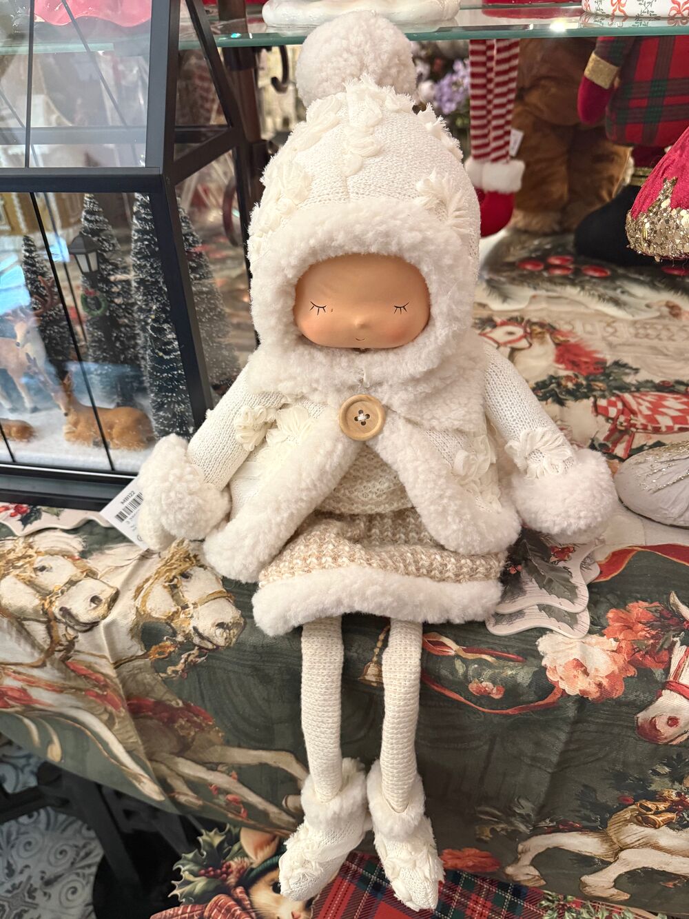 Grande poupée décorative d’hiver écrue et beige avec bonnet, tenue douillette et longues jambes, assise sur un meuble dans une ambiance shabby chic romantique