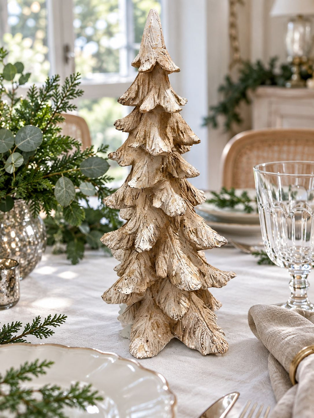 Sapin Roi des Neiges sur une table de fête en lin blanc, entouré de vaisselle et de feuillage vert.