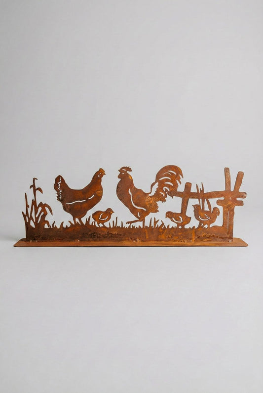 Silhouette décorative en fer forgé rouillé représentant une scène de basse-cour avec coq, poule et poussins, installée dans l’herbe d’un jardin champêtre