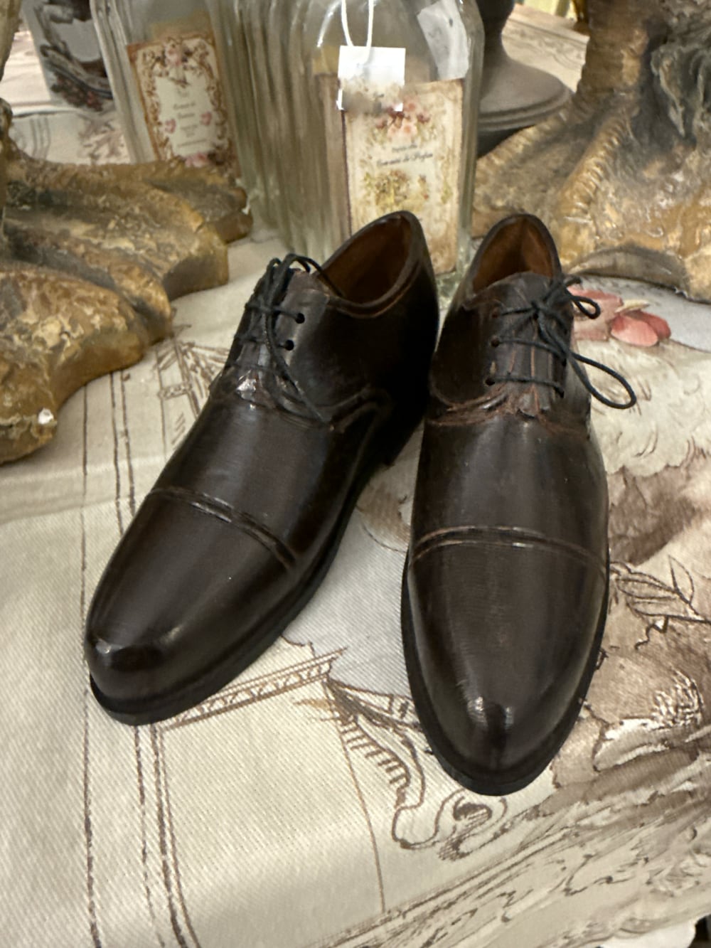 Paire de souliers décoratifs en métal noir patiné style ancien, posés sur un meuble de charme dans une ambiance vintage et romantique
