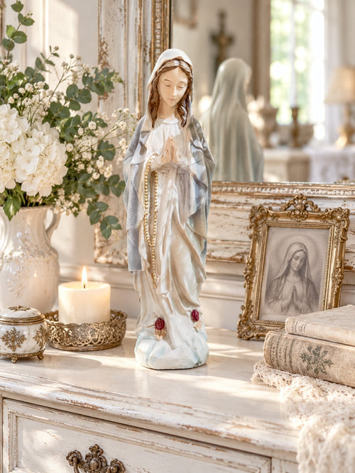 Statuette décorative de la Vierge Marie en prière tenant un chapelet doré, finitions nacrées blanc cassé, détails roses à la base, style romantique et shabby chic, ambiance spirituelle et poétique