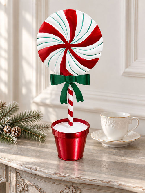 Sucette décorative de Noël de 31 cm à fins filets verts sur une console patinée près d’une tasse blanche.