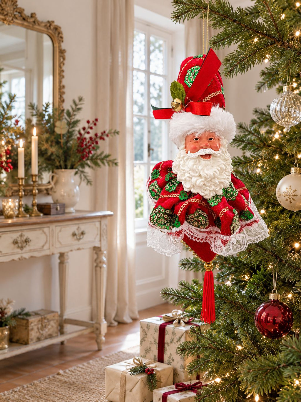 Suspension Père Noël dans un sapin décoré, près d’une console ivoire et d’un miroir ancien dans un salon lumineux.