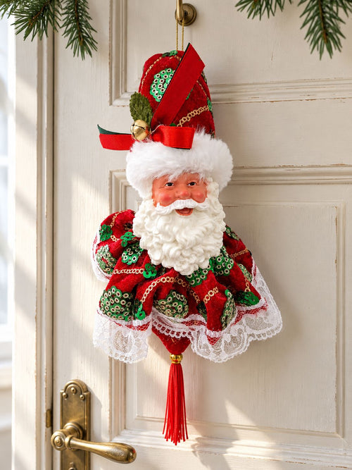 Suspension Père Noël avec dentelle blanche et pompon rouge, accrochée à une porte ancienne ivoire éclairée par la lumière du jour.