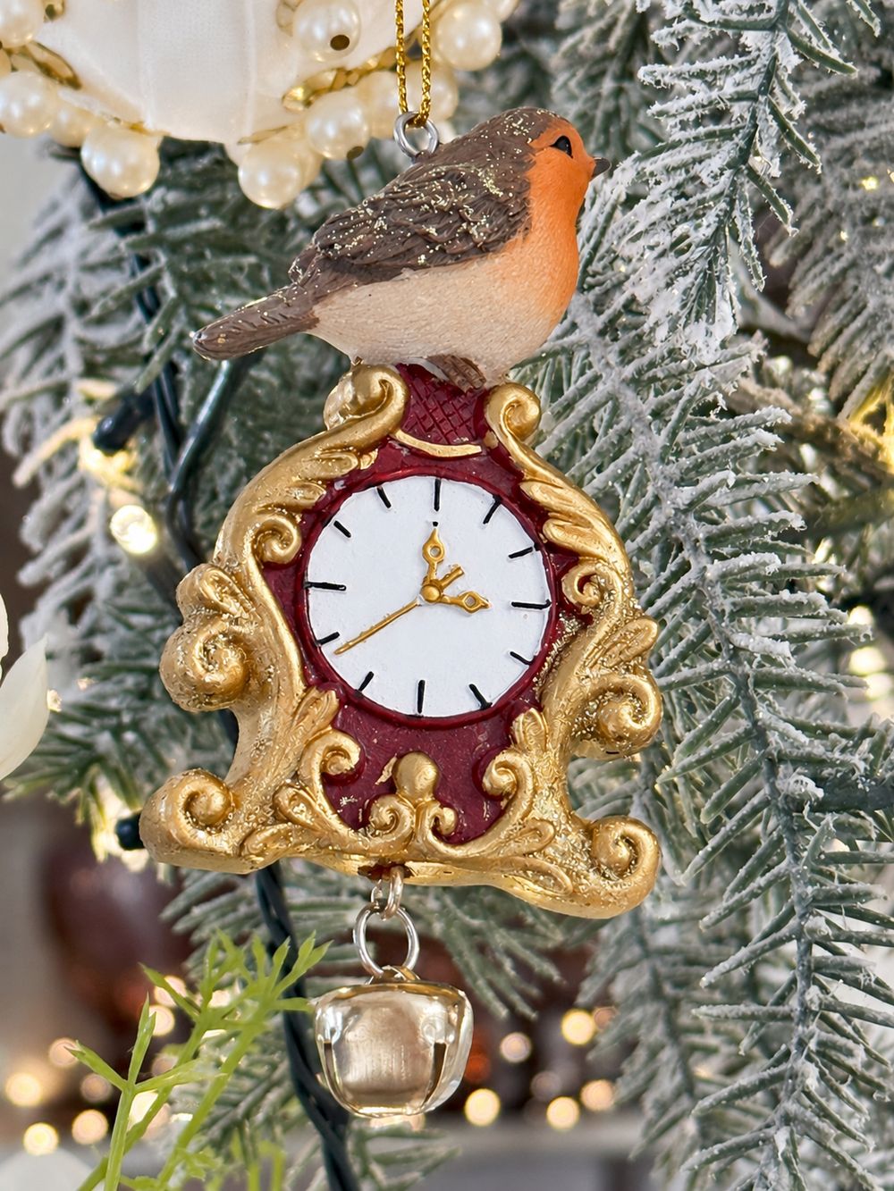 Suspension rouge-gorge sur horloge rouge et dorée avec grelot dans un sapin givré.