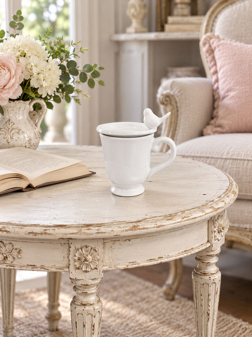 Tasse blanche fermée par sa coupelle oiseau, sur une table près d’un livre et d’un fauteuil.