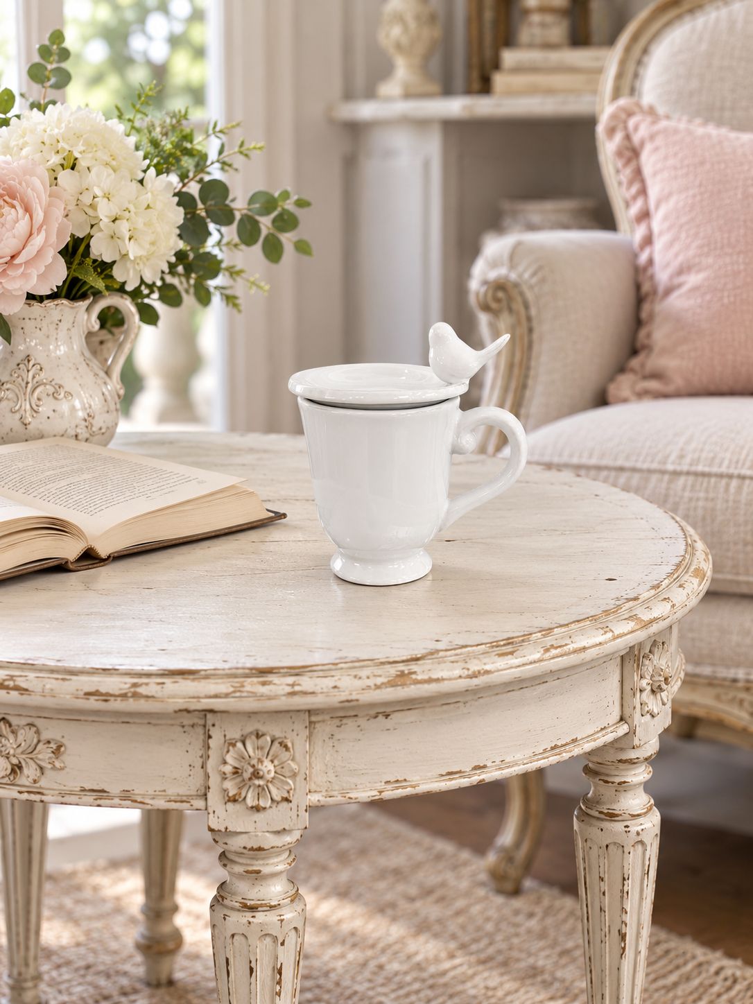Tasse blanche fermée par sa coupelle oiseau, sur une table près d’un livre et d’un fauteuil.