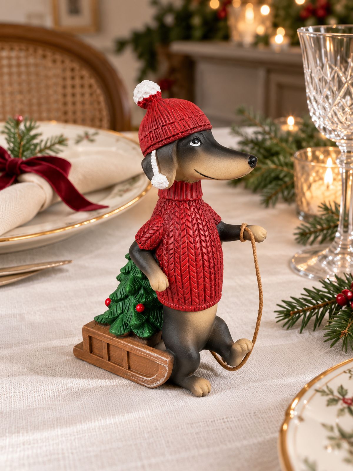 Figurine Teckel des Neiges sur une table de Noël en lin blanc, entourée de vaisselle ancienne et de branches de sapin.