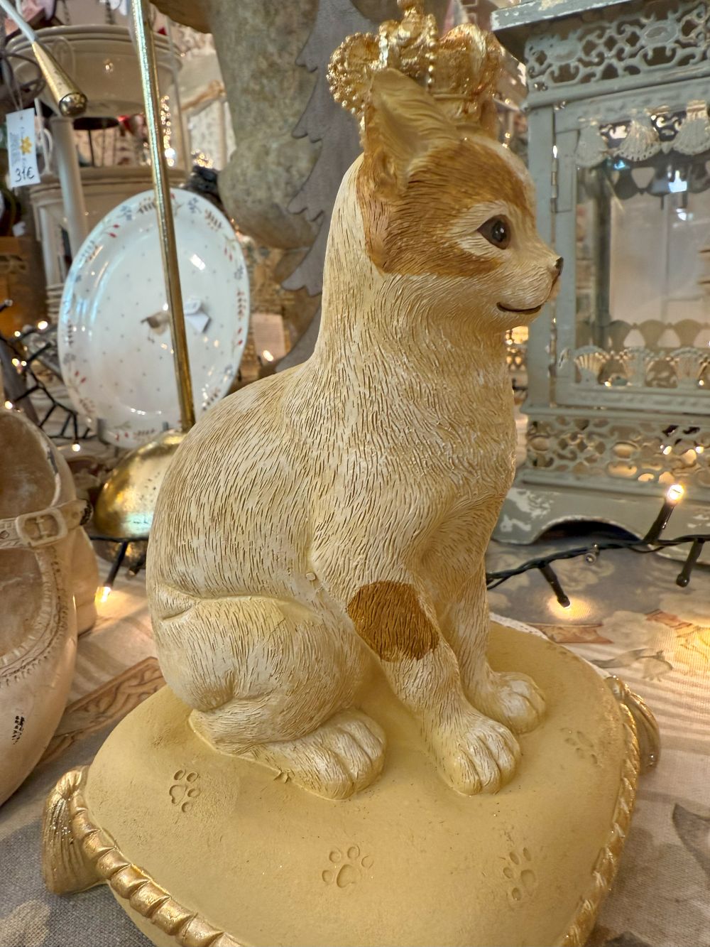 Tirelire décorative en forme de chat couronné, couleurs beige, doré et marron, style shabby chic romantique et poétique, posée sur un coussin élégant