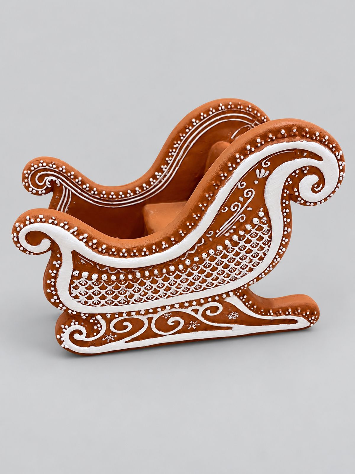 Traîneau décoratif en résine façon pain d’épices, brun à motifs blancs, présenté sur fond gris clair.