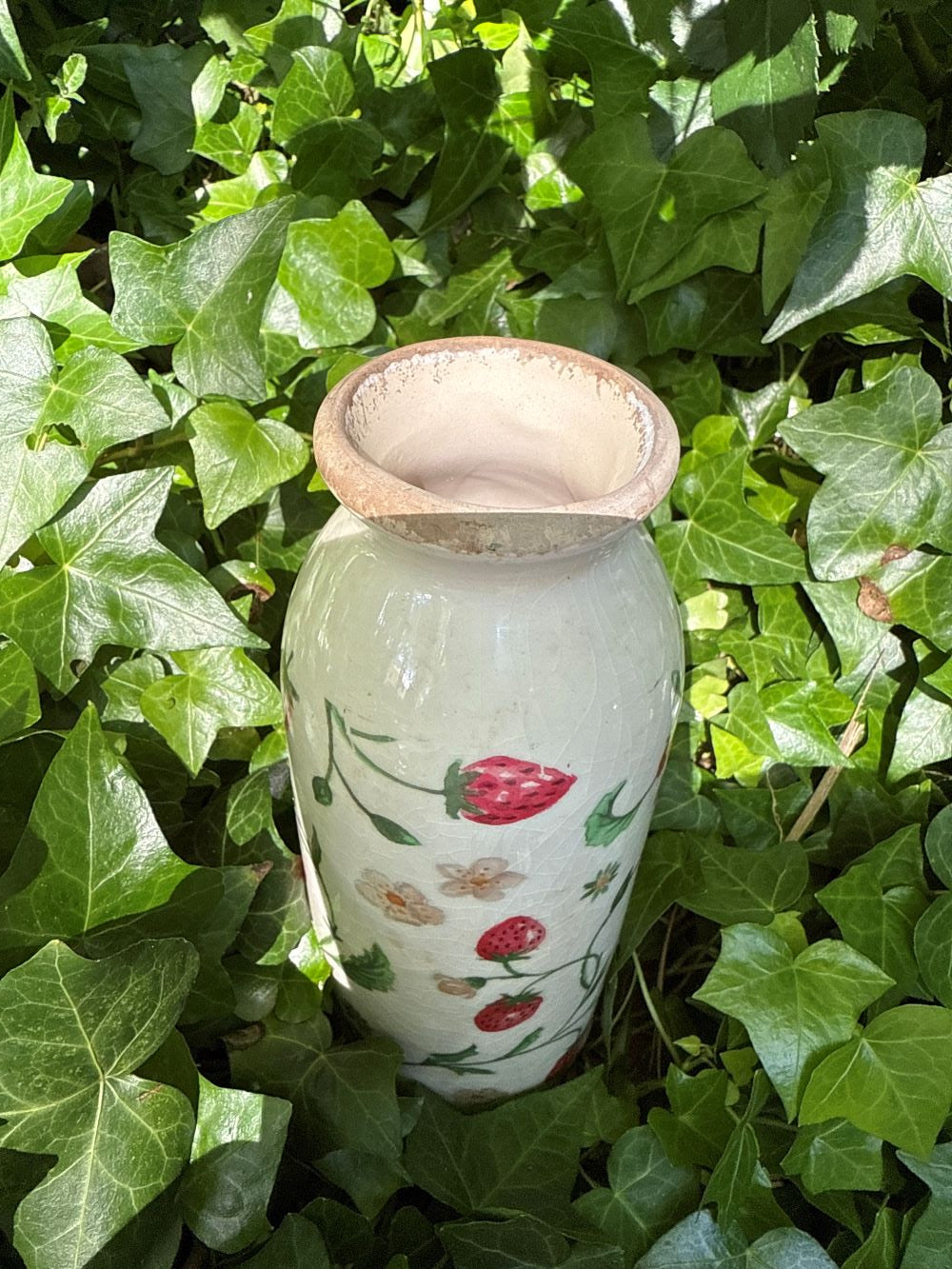 Vase décoratif en céramique blanc cassé avec motifs de fraises et fleurs, style shabby chic, ambiance romantique et bucolique, couleurs rouge, vert et blanc.