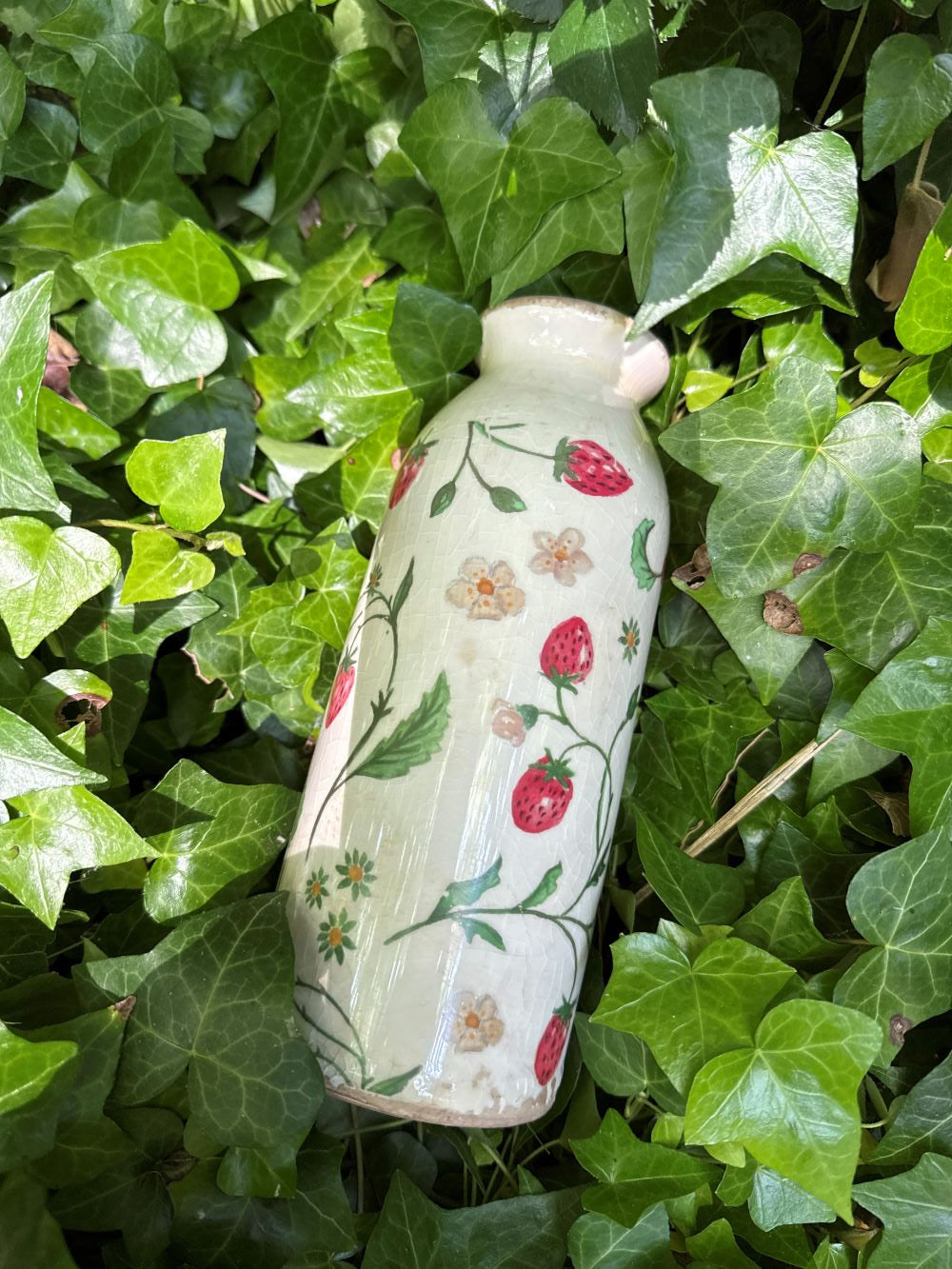 Vase décoratif en céramique blanc cassé avec motifs de fraises et fleurs, style shabby chic, ambiance romantique et bucolique, couleurs rouge, vert et blanc.